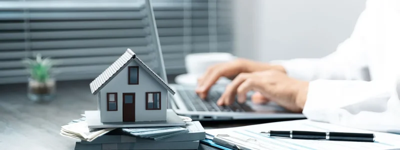 Miniaturhaus auf Aktenstapel vor Laptop – Hausverwaltung